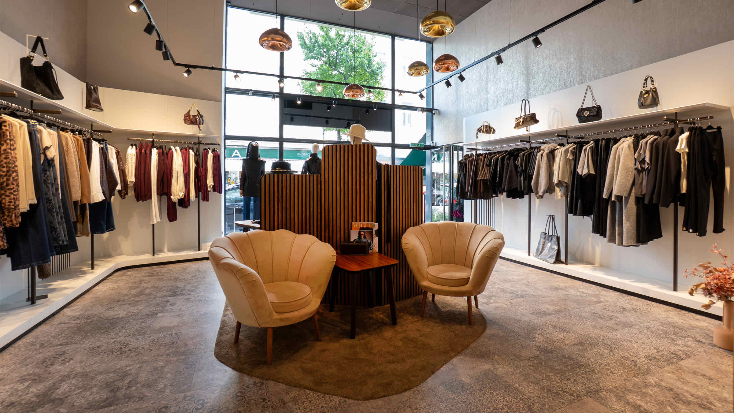 Innenraum der LIMAA Boutique in Baden: helle Verkaufsfläche mit Kleiderstangen, zwei cremefarbenen Samtsesseln um einen Beistelltisch und Kupferleuchten