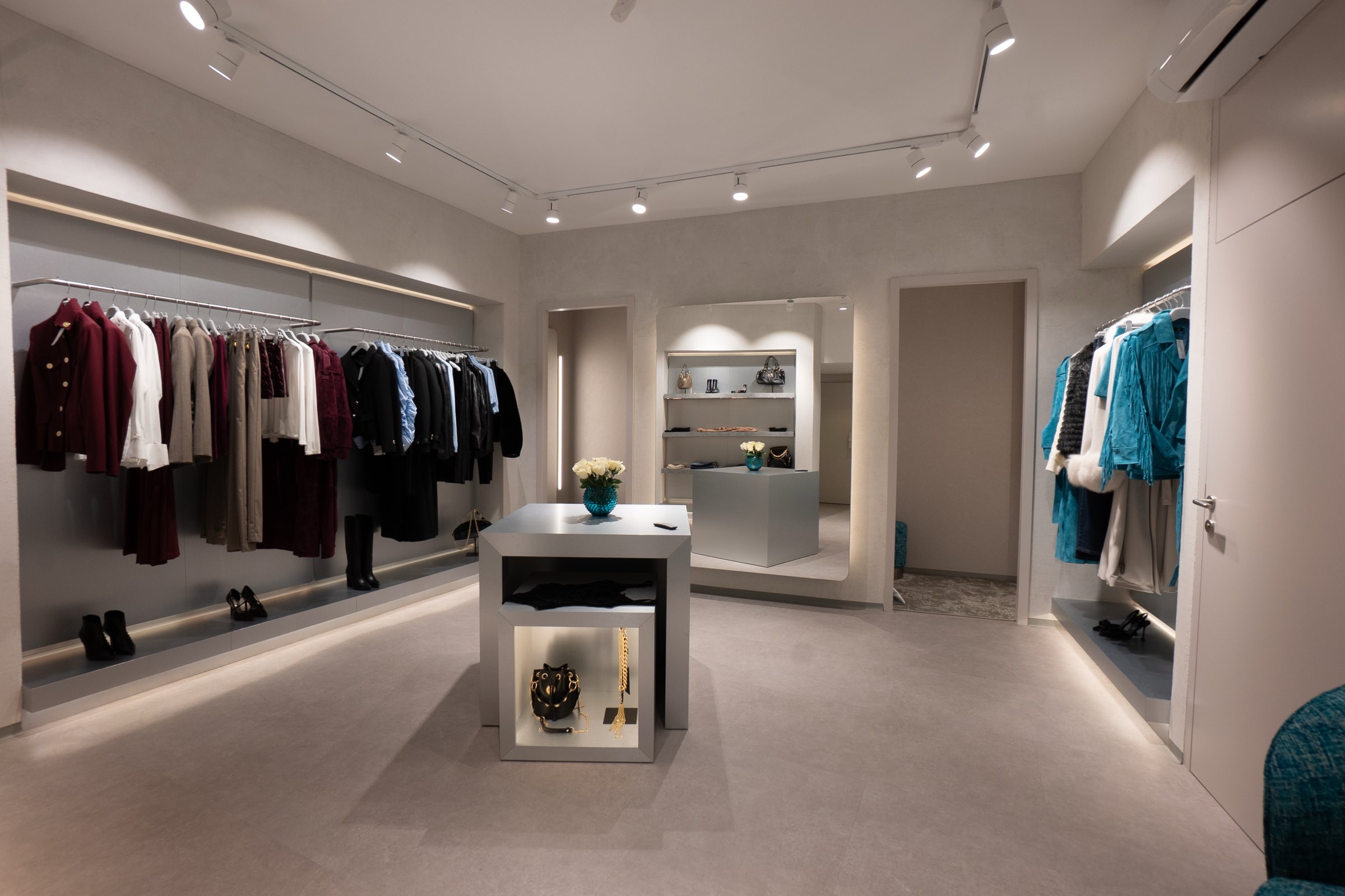 Weiter Blick in die Wiener LIMAA Boutique mit Kleiderstangen an beiden Wänden, beleuchteten Nischen und einem grauen Display-Würfel mit Schmuck und Blumen